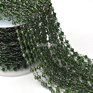 May include: A close-up of a green crystal bead chain with a silver chain. The chain is coiled and ready to be used for jewelry making.