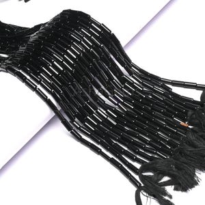 May include: Strands of glossy black beads, each a small, rectangular tube. The beads are strung together, forming multiple lines that cascade downwards. The ends of the strands are finished with black tassels, creating a dramatic effect.
