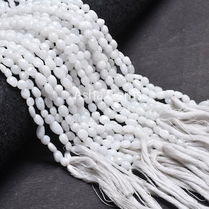 Puede incluir: Una hebra de cuentas de piedras preciosas blancas, con un borla al final. Las cuentas son de forma ovalada y tienen un acabado liso y pulido.