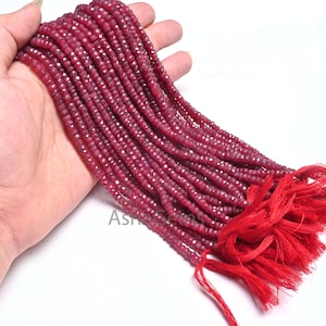 Könnte beinhalten: Eine Strähne tief roter Rubinperlen, jede Perle ist facettiert und hat einen Durchmesser von etwa 3 mm. Die Perlen sind auf einem dünnen Faden aufgefädelt und haben einen roten Quasten am Ende.