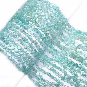 May include: A strand of light blue aquamarine gemstone beads. The beads are faceted and have a slightly irregular shape. The beads are strung on a clear thread.