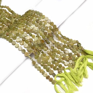 以下が含まれることがあります： 平らな円盤状のオリーブグリーンの宝石ビーズのストランド。ビーズは一緒に紐で繋がれ、端は明るい緑色のタッセルで仕上げられています。ビーズは自然で素朴な外観をしています。