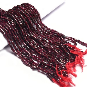 Op de afbeelding: Strengen donkerrode granaat edelsteen kralen. De kralen zijn rechthoekig en aan elkaar geregen, met een kwast van rode draad aan het einde van elke streng. De kralen hebben een diepe, rijke kleur en het algehele effect is elegant en opvallend.