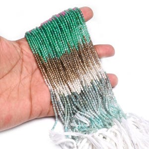 Puede incluir: Una colección de múltiples hilos de pequeñas cuentas de piedras preciosas facetadas dispuestas en un patrón de degradado de color. Las cuentas transicionan de verde vibrante y rosa arriba, pasando por tonos marrones y blancos, a azul claro y turquesa.