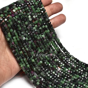 Może przedstawiać: Szereg zielonych i czarnych fasetowanych koralików z kamieni szlachetnych. Koraliki mają kwadratowy kształt i polerowane wykończenie.