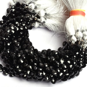 Puede incluir: Una hebra de cuentas de piedras preciosas negras, probablemente espinela negra, con forma irregular facetada. Las cuentas están enhebradas en un hilo blanco y están listas para ser utilizadas en la elaboración de joyas.