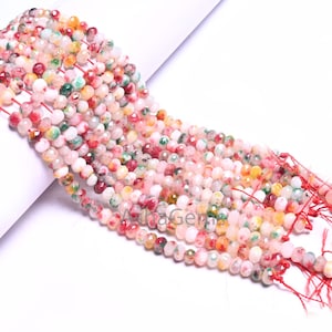 Może przedstawiać: Szereg wielokolorowych koralików z kamieni szlachetnych. Koraliki są okrągłe i mają nakrapiane, zamglone wykończenie. Kolory obejmują różowy, biały, czerwony, żółty i zielony.