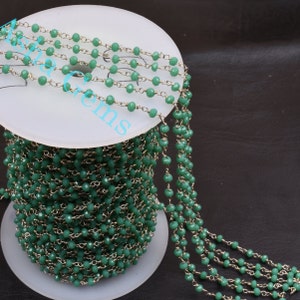 May include: A spool of green glass beads strung on a silver chain. The beads are faceted and have a light green color.