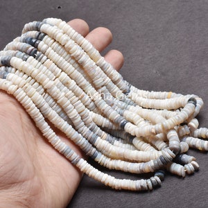May include: A strand of white and gray shell beads. The beads are small and round, and they are strung together on a thin thread. The beads are arranged in a loose, flowing pattern.