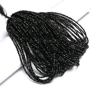 May include: A large bundle of small, shiny black beads. The beads are strung together, forming multiple strands. The image is taken on a white surface, with the beads cascading down. The beads are likely for jewelry making.