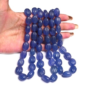 Könnte beinhalten: Eine Kette aus ovalen, tiefblauen Perlen. Jede Perle hat eine gerippte Textur und eine polierte Oberfläche. Die Perlen sind aufgefädelt und bilden eine Halskette oder ein Armband. Die Farbe ist ein sattes, gesättigtes Blau.