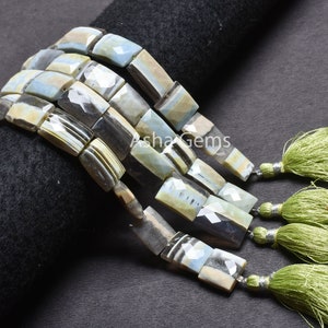 Puede incluir: Primer plano de un collar de cuentas rectangulares de piedras preciosas en tonos azules, grises y crema, con una superficie facetada. Las cuentas están ensartadas y terminadas con borlas verdes.