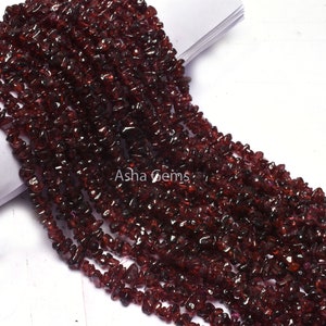 May include: A strand of small, irregular, dark red garnet gemstone chips. The chips are strung together to create a long, continuous strand of beads.