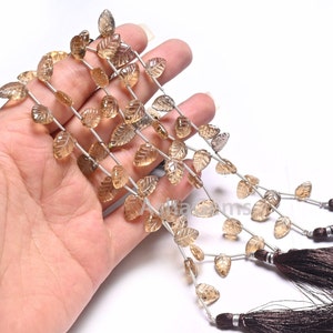 Può includere: Una collana di perle di pietra preziosa marrone a forma di foglie. Le perle sono infilate su un filo d'argento e hanno un aspetto naturale e traslucido. La collana è rifinita con nappe marroni.