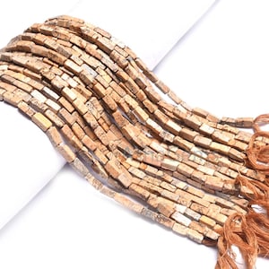 Puede incluir: Cadenas de cuentas rectangulares de color marrón claro, con una mezcla de tonos beige y blanco. Las cuentas están ensartadas, con una borla de hilos marrones al final de cada cadena. Ideales para la creación de joyas.