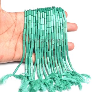 Könnte beinhalten: Stränge zylinderförmiger, türkisfarbener Perlen mit passenden Quasten. Die Perlen sind eine Mischung aus hellen und dunklen Türkistönen. Die Quasten bestehen aus einem weichen, gefransten Material.