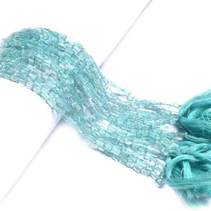 Puede incluir: Múltiples hebras de cuentas rectangulares de color azul claro, ensambladas en un conjunto. Un borla del mismo color completa el conjunto. Las cuentas parecen ligeramente translúcidas, creando un efecto de textura y movimiento.