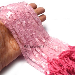 Puede incluir: Una hebra de cuentas de piedras preciosas rosadas y blancas, con forma rectangular, están enhebradas en un cordón con borlas rosadas en el extremo. Las cuentas están dispuestas en un degradado de rosa claro a blanco. Las cuentas se muestran en una mano.