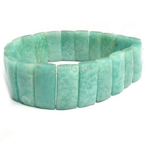 Puede incluir: Un brazalete turquesa hecho de piedras rectangulares. Las piedras están dispuestas en un bucle continuo, creando un accesorio flexible y ponible. El brazalete se muestra sobre un fondo blanco. Las piedras miden aproximadamente 1,5 cm de largo.