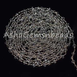 Könnte beinhalten: Eine lange Strähne aus klaren Kristallperlen, die auf einer silbernen Kette aufgefädelt sind. Die Perlen sind facettiert und funkeln im Licht.