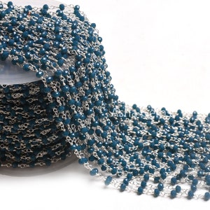 Peut inclure: Une chaîne de perles de couleur teal sur une bobine. Les petites perles à facettes sont enfilées sur une fine chaîne argentée. La chaîne est partiellement déroulée, révélant les détails du travail de perlage. Idéal pour la création de bijoux.