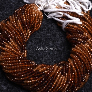 May include: A strand of brown gemstone beads, likely citrine, with a faceted finish. The beads are strung on a white thread and are arranged in a circular shape. The image includes the text "AshaGems".