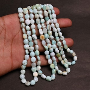 Op de afbeelding: Strengen lichtblauwe en witte edelsteen kralen. De ovale kralen zijn geregen, waardoor een halsketting- of armbandontwerp ontstaat. De kralen hebben een gepolijste afwerking en variëren in kleur, met strepen van donkerder blauw.