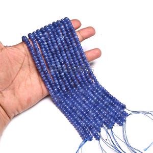 May include: Multiple strands of small, round, blue beads. The beads are strung together, creating several strands. The beads are a consistent size and colour, with a slightly matte finish. The background is white.