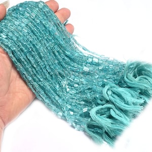 Puede incluir: Una hebra de cuentas de piedra preciosa de aguamarina azul claro, cada cuenta tiene forma rectangular. Las cuentas están enhebradas en un hilo fino y están listas para ser utilizadas en la elaboración de joyas.