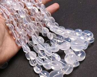 May include: A strand of translucent white gemstone beads, each bead is oval shaped and polished smooth. The beads are strung on a white cord and are arranged in a loose pile.