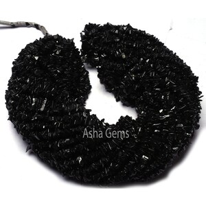 Peut inclure: Collier long composé de petites pierres précieuses noires en forme irrégulière. Le collier est disposé en forme de U sur un fond blanc.