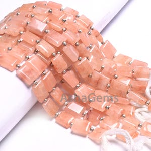 Puede incluir: Una hebra de cuentas de piedras preciosas de color melocotón con separadores plateados. Las cuentas son rectangulares y tienen un acabado liso y pulido. La hebra mide aproximadamente 45 cm de largo.
