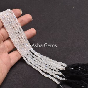 May include: A strand of white moonstone beads with a black tassel. The beads are faceted and have a subtle iridescent shimmer.