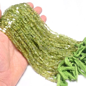 Peut inclure: Un ensemble de perles rectangulaires vert clair avec une légère teinte jaune. Les perles sont enfilées ensemble, avec un pompon vert à l'extrémité. Les perles sont tenues dans une main sur fond blanc.