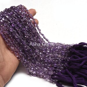 Könnte beinhalten: Eine Strähne aus violetten Amethyst-Edelsteinkugeln, jede Kugel hat eine glatte, ovale Form. Die Kugeln sind auf einer Schnur aufgefädelt und haben einen violetten Quasten am Ende.