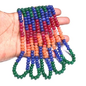 Peut inclure: Plusieurs colliers de perles multicolores, verts, bleus, rouges et oranges. Les petites perles rondes sont enfilées pour former plusieurs brins. Les colliers sont présentés sur un fond blanc.