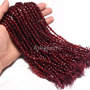 Puede incluir: Una hebra de cuentas de piedras preciosas de color rojo intenso, probablemente cornalina, de forma ovalada lisa. Las cuentas están enhebradas en un cordón fino y están listas para la elaboración de joyas.