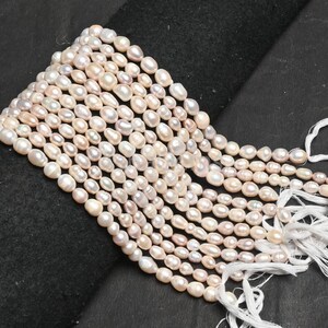 Puede incluir: Una hebra de perlas de agua dulce blancas y rosadas, enhebradas en un hilo blanco. Las perlas son de forma ovalada y tienen un acabado liso y brillante.