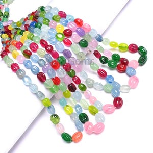 Puede incluir: Hebras de cuentas ovaladas multicolores, rojas, verdes, azules, rosas y amarillas. Las cuentas están ensartadas, creando una exhibición vibrante y llamativa. Estas cuentas son probablemente para la fabricación de joyas.