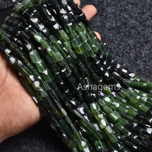 Puede incluir: Una hebra de cuentas de piedras preciosas facetadas de color verde oscuro y negro. Las cuentas son de forma rectangular y tienen un acabado pulido.