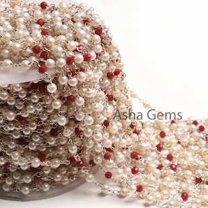 Könnte beinhalten: Eine Kette aus weißen Perlen und roten Edelsteinen mit einer silbernen Kette. Die Kette ist um eine Spule gewickelt. Der Text "Asha Gems" ist auf der Spule sichtbar.