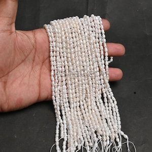 Puede incluir: Un largo hilo de pequeñas perlas de agua dulce blancas de forma irregular, dispuestas en varias filas verticales. Las perlas tienen un acabado lustroso de color blanco roto y están ensartadas en hilos blancos finos, creando una apariencia texturizada en cascada.