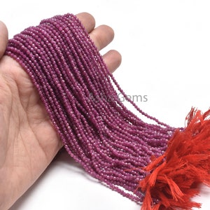 May include: A strand of pink ruby beads, approximately 2 mm in size, with a red tassel. The beads are faceted and have a shiny finish.