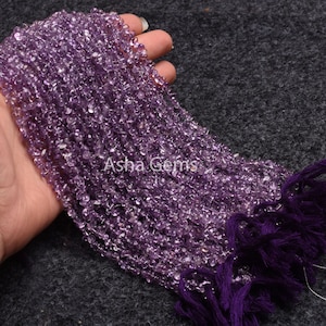 Könnte beinhalten: Eine Strang aus Amethyst-Edelsteinen, facettierten und mit einem hellvioletten Farbton. Die Perlen sind auf einem Faden mit einem violetten Quasten am Ende aufgereiht. Die Perlen sind etwa 4 mm groß. Asha Gems.