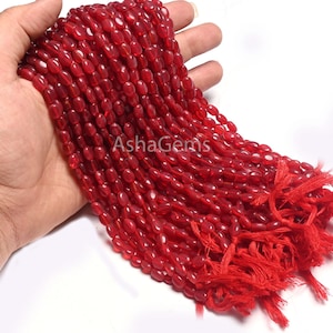Puede incluir: Una hebra de cuentas de piedras preciosas rojas, de forma ovalada, con un borla roja en el extremo. Las cuentas están enhebradas en un cordón fino y tienen un tamaño aproximado de 10 mm.