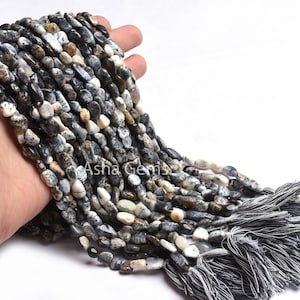 Könnte beinhalten: Eine Schnur aus schwarzen und weißen Opal-Edelsteinen mit einer rauen, unregelmäßigen Form. Die Perlen sind auf einer Schnur aufgefädelt und haben einen Quasten am Ende.