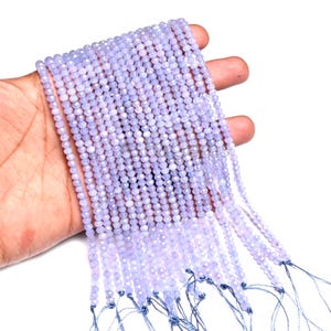 Könnte beinhalten: Eine Handvoll hellvioletter, facettierter Edelsteinperlen. Die Perlen sind auf dünnen, dunkelblauen Schnüren aufgefädelt. Die kleinen, runden Perlen haben eine weiche, pastellviolette Farbe.