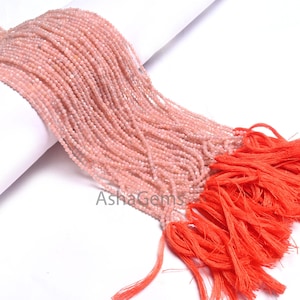 Op de afbeelding: Een streng roze opaal kralen, ongeveer 2 mm in diameter, met een kwast aan het einde. De kralen zijn geregen op een doorzichtige draad en zijn klaar om te worden gebruikt voor het maken van sieraden.