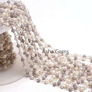 Könnte beinhalten: Eine silberne Kette mit abwechselnd grauen und weißen Perlen. Die Kette ist auf einer weißen Oberfläche aufgewickelt. Der Text "Asha Gems" ist im Bild sichtbar.