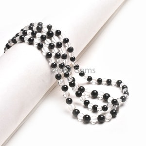 May include: A strand of black and clear round beads. The beads are strung on a white cord and are arranged in a alternating pattern.